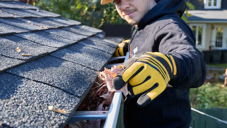 Installer clearing leaves from a gutter system on a residential job