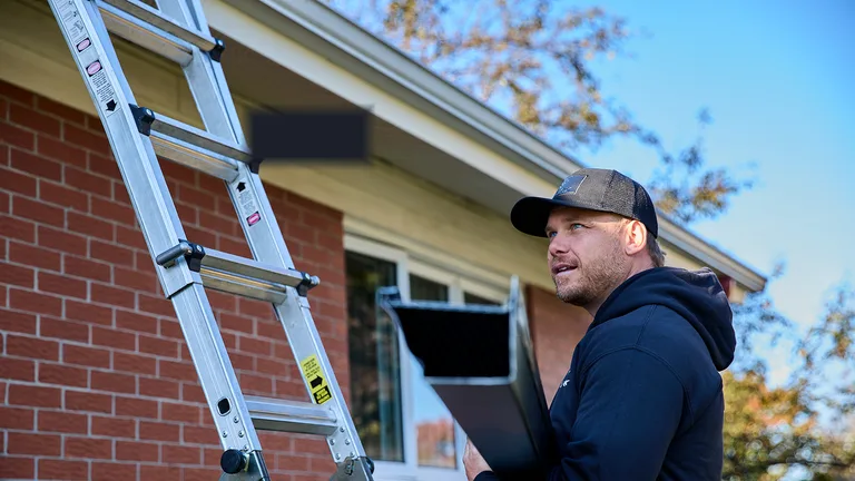 Installer reviewing a gutter estimate on a clipboard at the ladder
