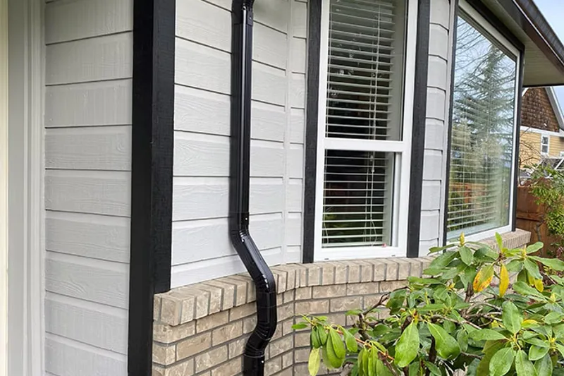 New black aluminum downspout installed on white siding