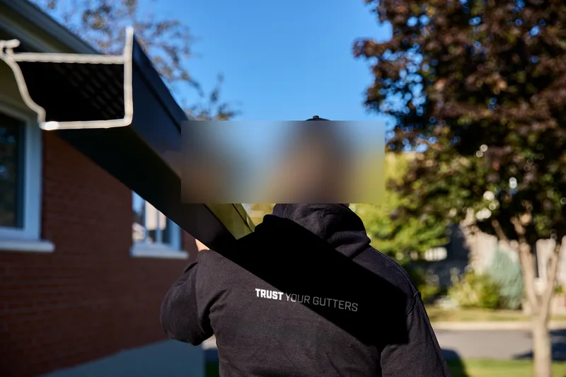 Installer securing a white downspout elbow on a residential gutter system