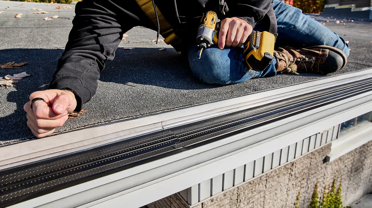 Installer fastening a gutter at the roof edge with a drill