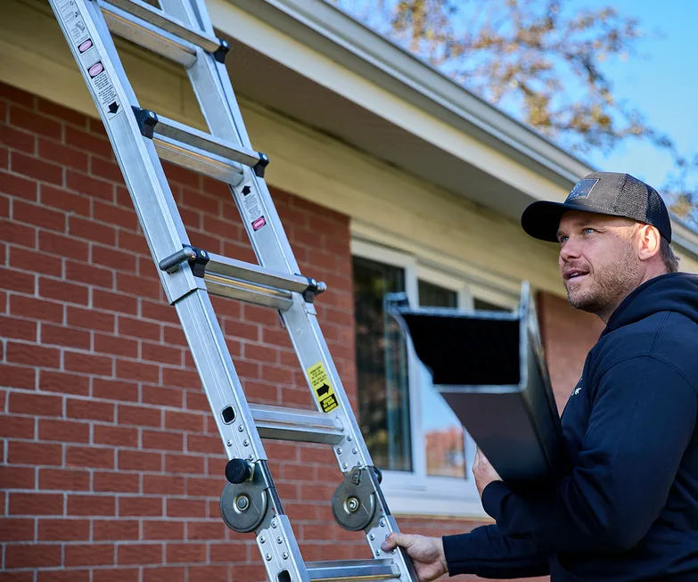Installer carrying a new seamless gutter up a ladder