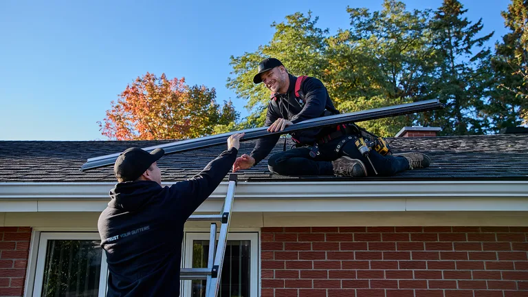 Two installers carrying a seamless gutter up to the roof