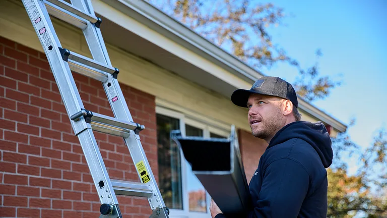 Installer carrying a new seamless gutter up a ladder